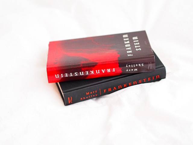 Two copies of Frankenstein by Mary Shelley sit one on top of the other on a white background. The top copy has a red and black jacket, while the bottom copy has a plain black cover.